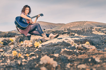 Woman playing a blue guitar sitting on a stone.の写真素材