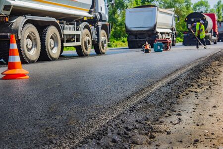 Close up of a new road and paving machine on it that was recently paved with builders in uniform on the back fon.の写真素材
