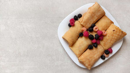 Pancakes with berries with filling on a white plate close-up on a white table with glass, top view, pancakes rolled up in an envelope, homemade foodの写真素材