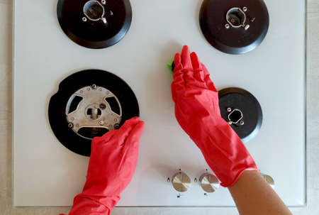 Cleaning the white hob with red rubber protective gloves with a green washcloth, first-person view. First person cleaning in the kitchen top viewの写真素材