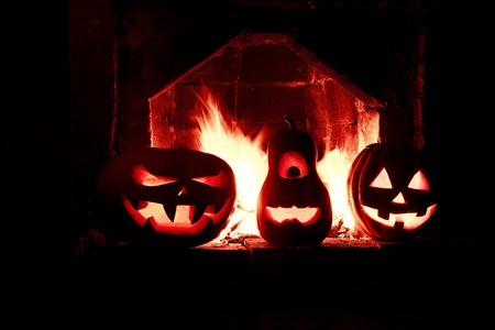 halloween three pumpkins at the fireplace with a fire in the dark isolated in redの写真素材