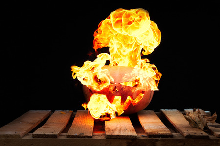 Halloween pumpkin on the boards with a large real fire erupting from it in the form of a nuclear explosion on a black backgroundの写真素材