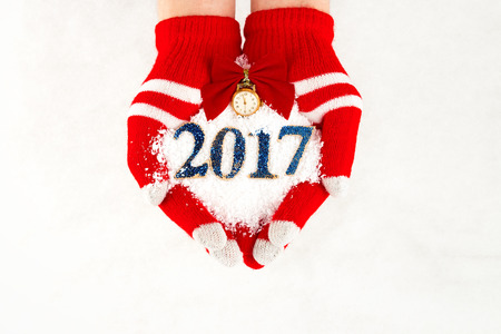 Christmas card, gloves on hands holding snow clock with time  five to midnight and 2017 new year...