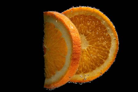 Fresh orange slice in water with bubbles on black gradient backgroundの写真素材