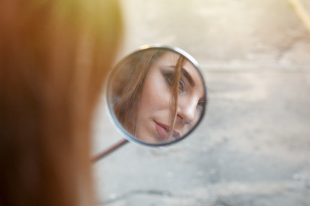 Reflection of a beautiful girl in a motorcycle moped rearview mirrorの写真素材