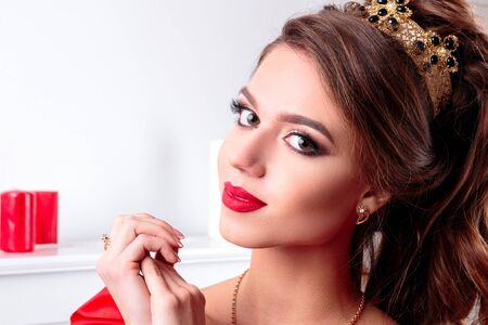 Beautiful elegant girl in a long red dress and shoes is standing next to the piano in a white room a large portrait of a girl with makeup and a hairdoの写真素材