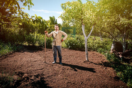 Farmer working in the garden with the help of a rake leveling plowed land, on a sunny dayの写真素材
