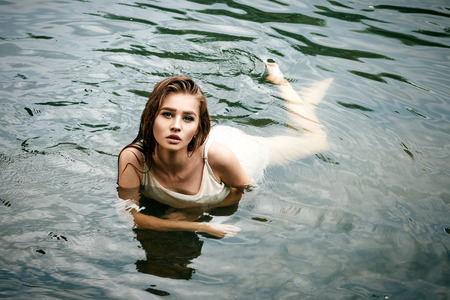 Passionate sexy female girl, dressed in a light negligee, bathes lies in the river wet and very beautifulの写真素材