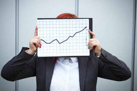 Business concept of success and growth. A successful woman boss, in a suit and wearing glasses, holds a tablet with charts of growth and achievements. With a place for advertising text. Chef Day, Boss Dayの写真素材