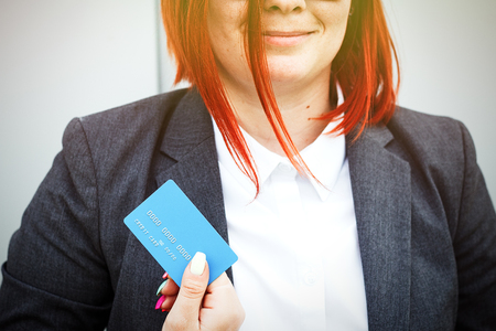 Concept of purchases, banking services. A woman in a suit and glasses shows a credit card. With a place for advertising text.の写真素材
