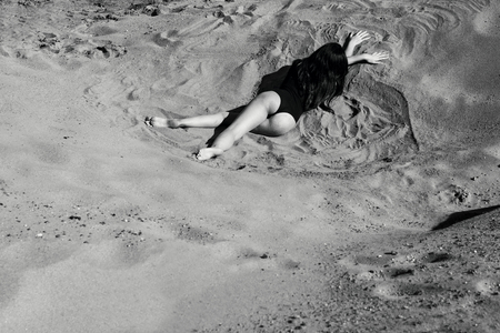 Sexy woman or girl in seductive sexy body suit lying on the sand in the desert or on the beach. Concept of leisure, travel and vacation. monochrome black and white pictureの写真素材