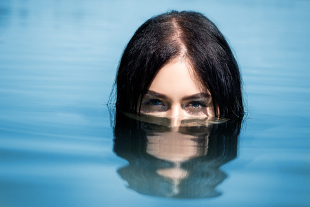 A sexy woman or girl, floating in the water, only the eyes are visible from the water. Concept of leisure, travel and vacationの写真素材
