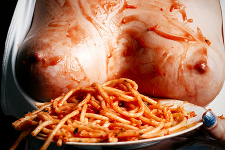 Naked breast of the girl smeared with ketchup and pasta, next to a plate of spaghetti in sauceの写真素材