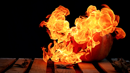 A very dangerous dangerous Halloween pumpkin, with a stern gaze and a smirk of a villain, in the darkness on a wooden pallet, spouts out the mouths and eyes of the flames of fire.の写真素材