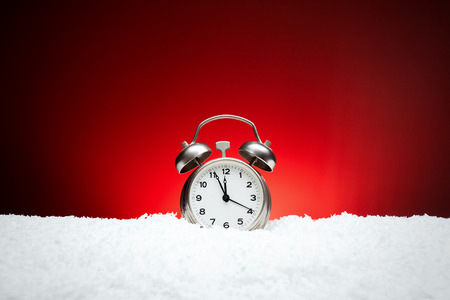 Christmas composition. Greeting card for new year clock Alarm clock on snow on red background with place for congratulatory textの写真素材