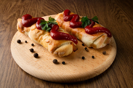 Delicious appetizing strudels on a wooden board with parsley, poured with ketchup and pepperの写真素材