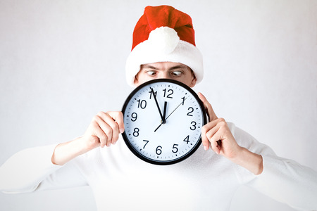 A stylish guy in a santa hat celebrates Christmas and a new year. A man holds a watch at midnight and goes crazyの写真素材