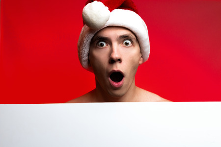 Christmas New Year concept, Stylish guy santa hat very surprised with white paper bottom and red glow background with place for textの写真素材