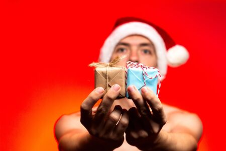 Christmas holiday presents. Man hold New year gift. Stylish guy in santa claus hat very happy on red background, give surprise conceptの写真素材