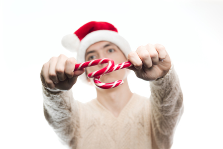 Christmas new year concept food and sweets. Man in santa claus hat holding many candies stick. Stylish happy guy lick a lot of candy cone on white backgroundの写真素材