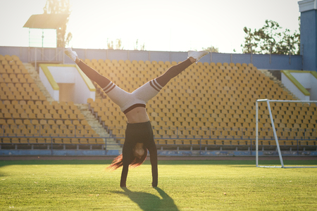 fitness girl on stadium, sporty women in sport suit, do exercises on sunny day. Sexy brunette with muscles body posing. female walks on hands grassの写真素材