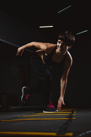 fitness girl doing crossfit exercises in gym in dark hall, sporty woman sexy in pose doing functional training, poster banner healthy lifestyleの写真素材