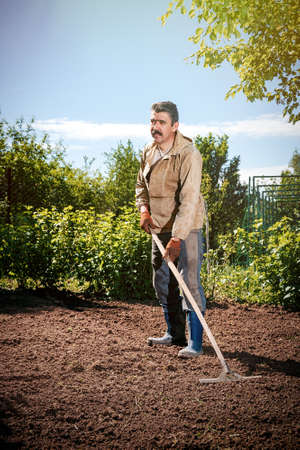 Farmer working in the garden with the help of a rake leveling plowed land, on a sunny dayの写真素材