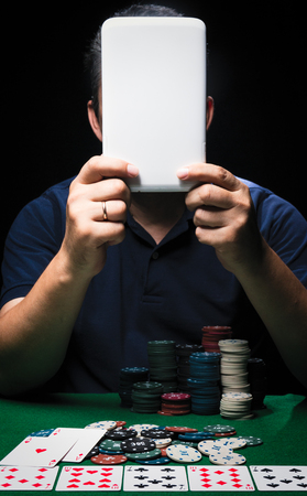 Man is playing poker with tablet online. Emotional  card player win in game, man very happy with making right choices, winning all the chips on bank. Concept of victory and internet online gameの写真素材