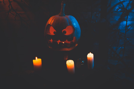 Concept of Halloween. glowing orange and blue light with angry terrible pumpkin, leaves, jack-lamp with candle of a happy Halloween, on a wooden backgroundの写真素材