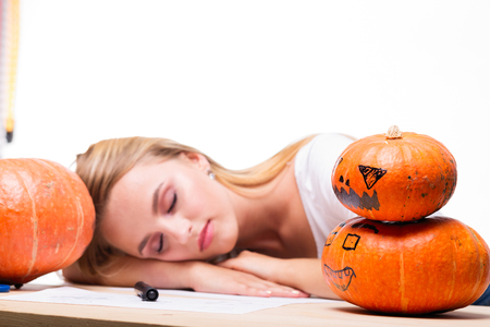 Halloween concept, happy Girl sitting at table with pumpkins preparing for holiday with candle and rope, sleeping on table near Jack lantern, funny and spooky pumpkin. Trick or treat traditionの写真素材