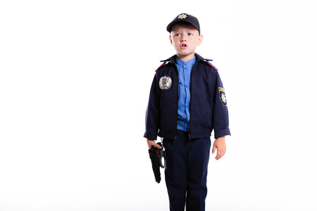 Cute sad little police boy with smile on face and gun on white background. Intelligent cool children in police suit with blue eyes and weaponの写真素材
