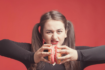 Model plus size with sweet donut, happy girl smiling holding in hands donuts and push them, in black bodysuit. XXL female on red backgroundの写真素材