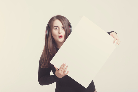 Model plus size with sweet donut, happy surprised girl posing with headphones listen music, in black bodysuit. XXL female on light background with white board for textの写真素材