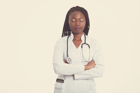 Female american african doctor, nurse woman wearing medical coat with stethoscope and tablet in poket. Serious excited for success medical worker posing on light backgroundの写真素材