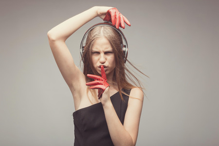 Fashion pretty girl listening music with headphones, wearing red gloves, take pleasure with song, and ask everybody to shut up, using her finger near mouth. Lifestyle woman conceptの写真素材