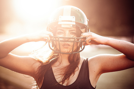 Sexy young sportive girl in uniform of rugby football player in action on the stadium. American...