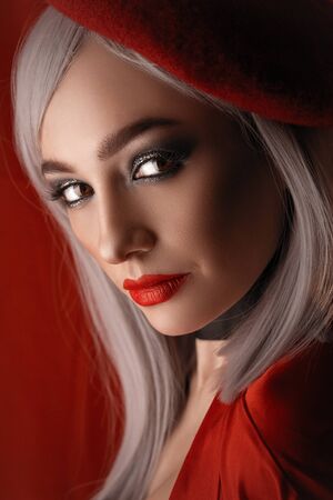 French girl in a red beret with red lips with big beautiful eyes in the interior loft studio. Woman in a red jacket. Fashionable female with white hairの写真素材