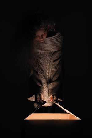 Merry Christmas and happy new year! happy girl near big present open it, and light from it blessing on her. Miracle in dark holiday time. Daughter open present from santa claus or parents.の写真素材