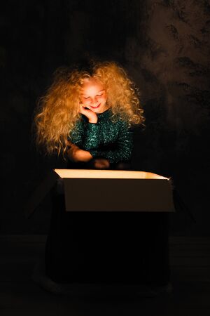 Merry Christmas and happy new year! happy girl near big present open it, and light from it blessing on her. Miracle in dark holiday time. Daughter with present from santa claus or parents.の写真素材