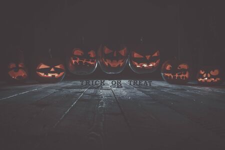 Concept of Halloween. Many glowing fiery light of evil scary pumpkins flying through the air. jack lantern, with the inscription trick or treat, with blue cool light behind on wooden backgroundの写真素材