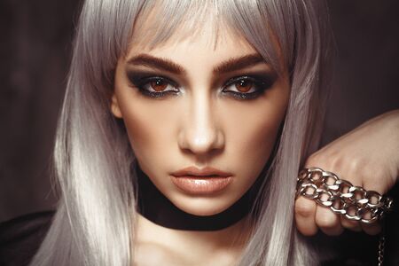 Girl in a leather jacket with white hair with big beautiful eyes in an interior loft studio with a chain in her hands. The girl in the bra. Fashionable Female stands at the brick. Fashionable female with gray hairの写真素材