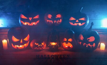 The concept of Halloween. Many Evil Scary Pumpkins in the dark with a blue ice glow. Jack Lantern amidst the darkness with a bat lamp, candles with an inscription of halloween and smokeの写真素材