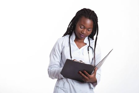 Female american african doctor, nurse woman wearing medical coat with stethoscope write good test results in hospital sheet chart. Happy excited for success medical worker posing on light backgroundの写真素材