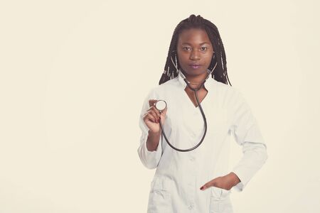 Female american african doctor, nurse woman wearing medical coat and using stethoscope. Serious excited for success medical worker posing on light background isolatedの写真素材