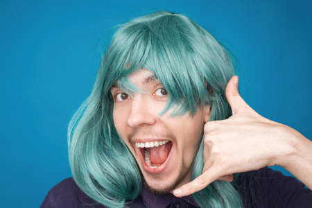 Funny portrait of a man with happy emotion on his face in the studio on blue background. Man wearing wig. Green hairの写真素材