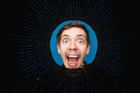 Man looking inside rounded tube. Close-up shot of happy shocked young man with round eyes and open mouth smile.の写真素材
