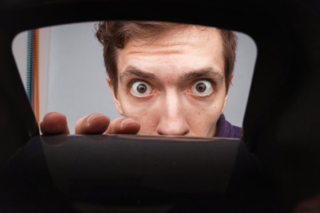 Man looking in plastic box with door. Close-up shot of shocked young man with round eyes.の写真素材