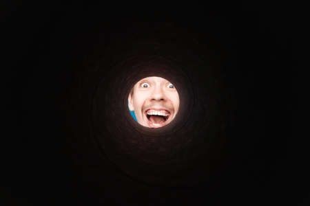 Man looking inside rounded tube. Close-up shot of happy shocked young man with round eyes and open mouth smile.の写真素材