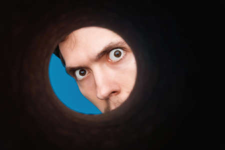 Man's eyes looking inside rounded tube. Empty place for a text or object. Close-up shot of shocked young man with round eyesの写真素材