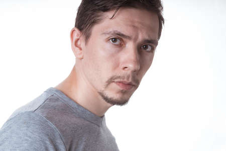 Portrait of a sensual young model in unlabeled gray t-shirt posing on white background. Serious man with small beard close-up portraitの写真素材